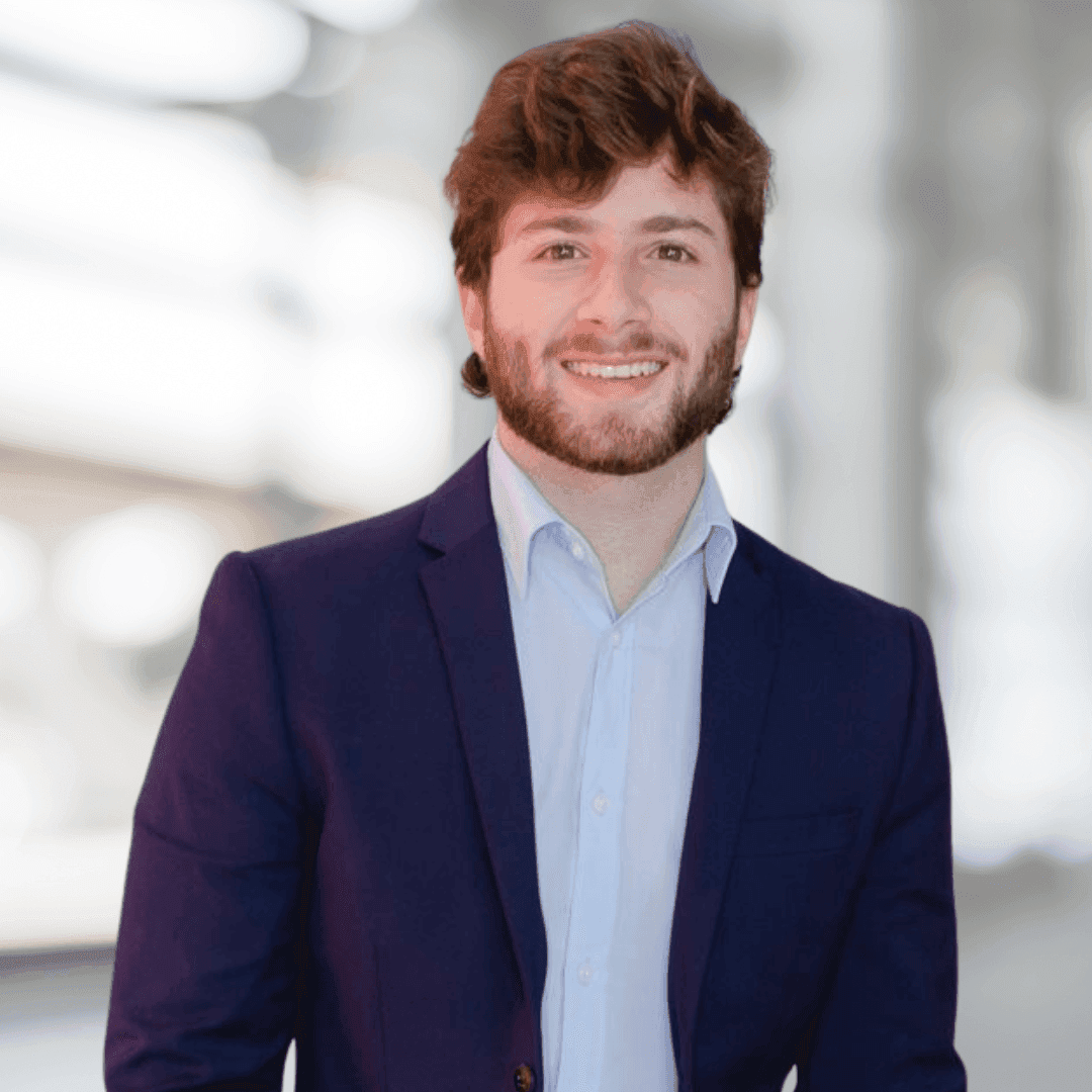 Person wearing a dark blue blazer and light blue shirt in a softly lit indoor setting.