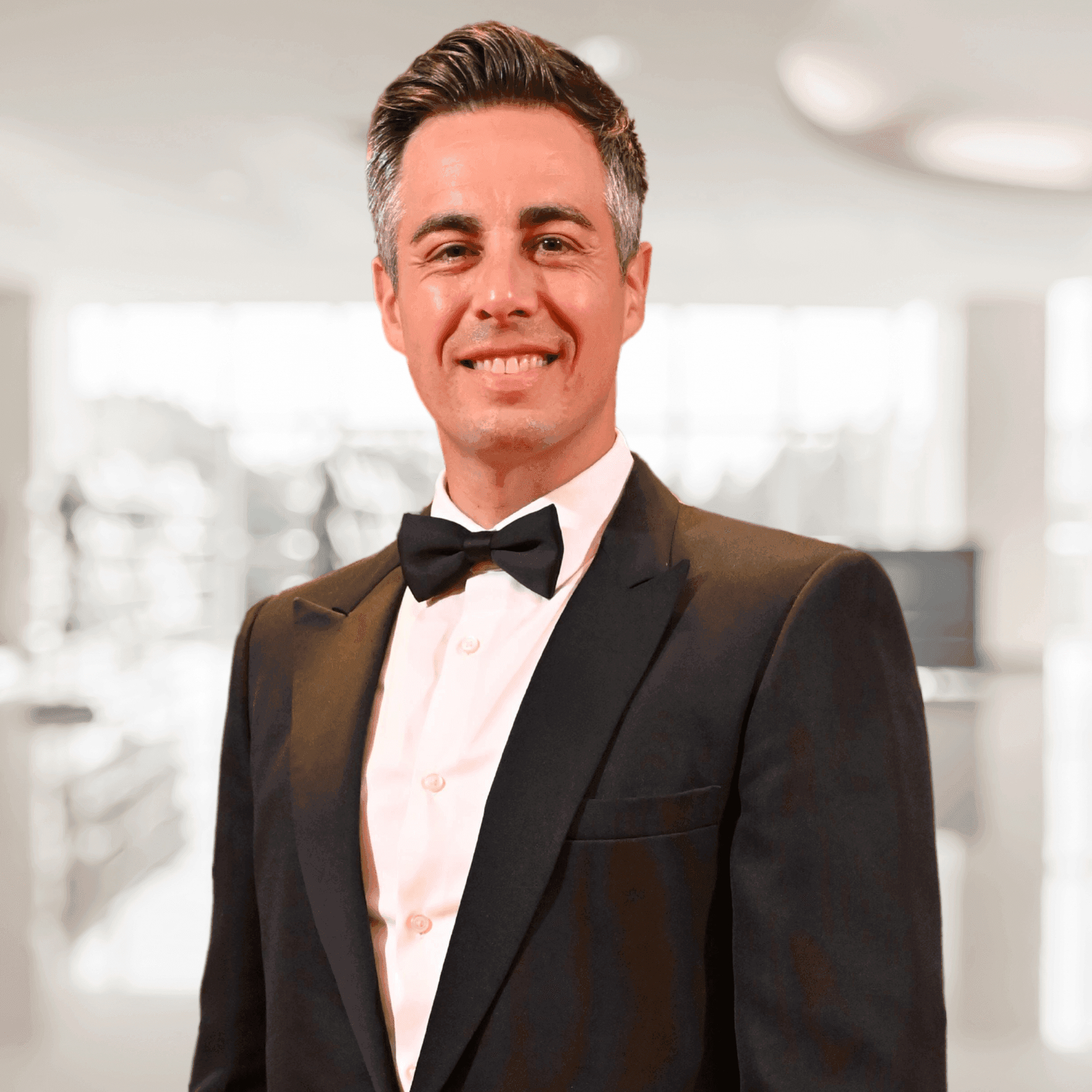 Man wearing a tuxedo with a bow tie in a bright indoor setting.