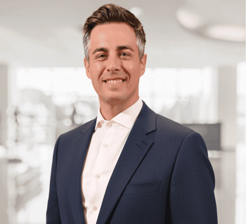 Smiling man in a suit with a blurred office background.