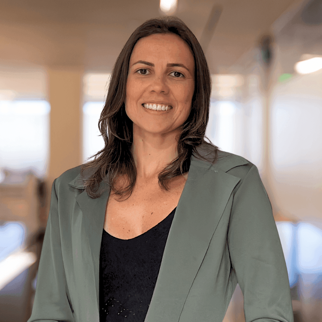 Smiling woman in a green blazer standing indoors in an office setting.