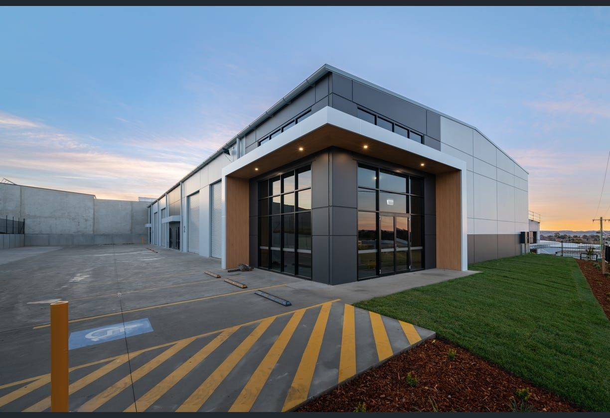 Modern industrial building with large windows and an empty parking lot, under a clear sky at sunset.