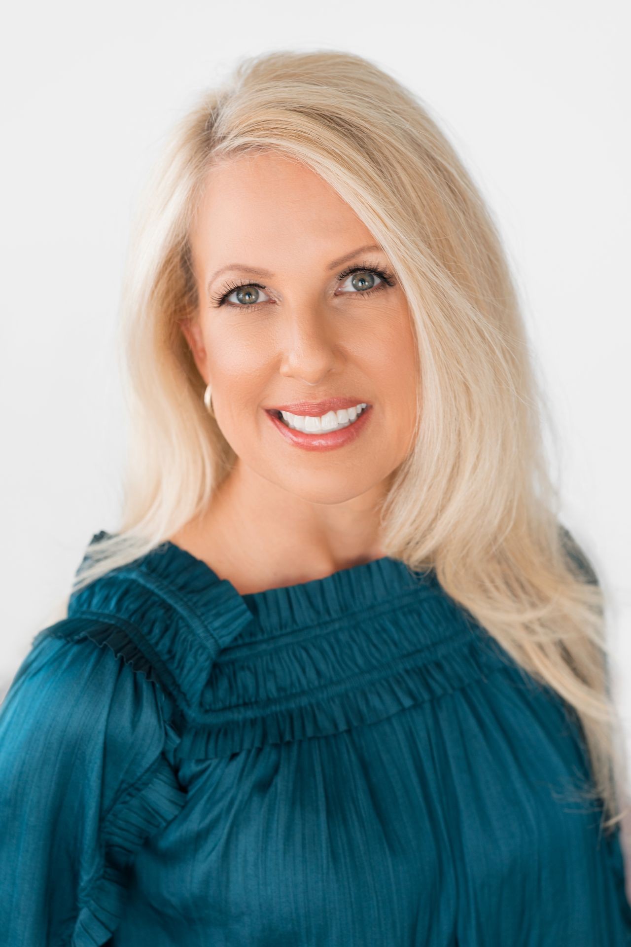 Person with long straight blonde hair wearing a teal-colored blouse with ruffled details.